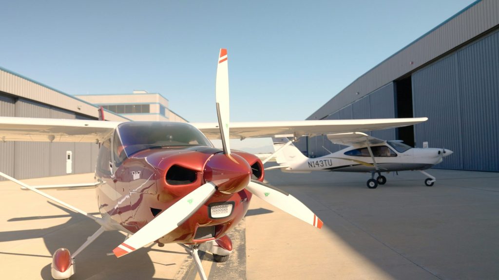 Deux petits avions stationnés devant des hangars par une journée ensoleillée.